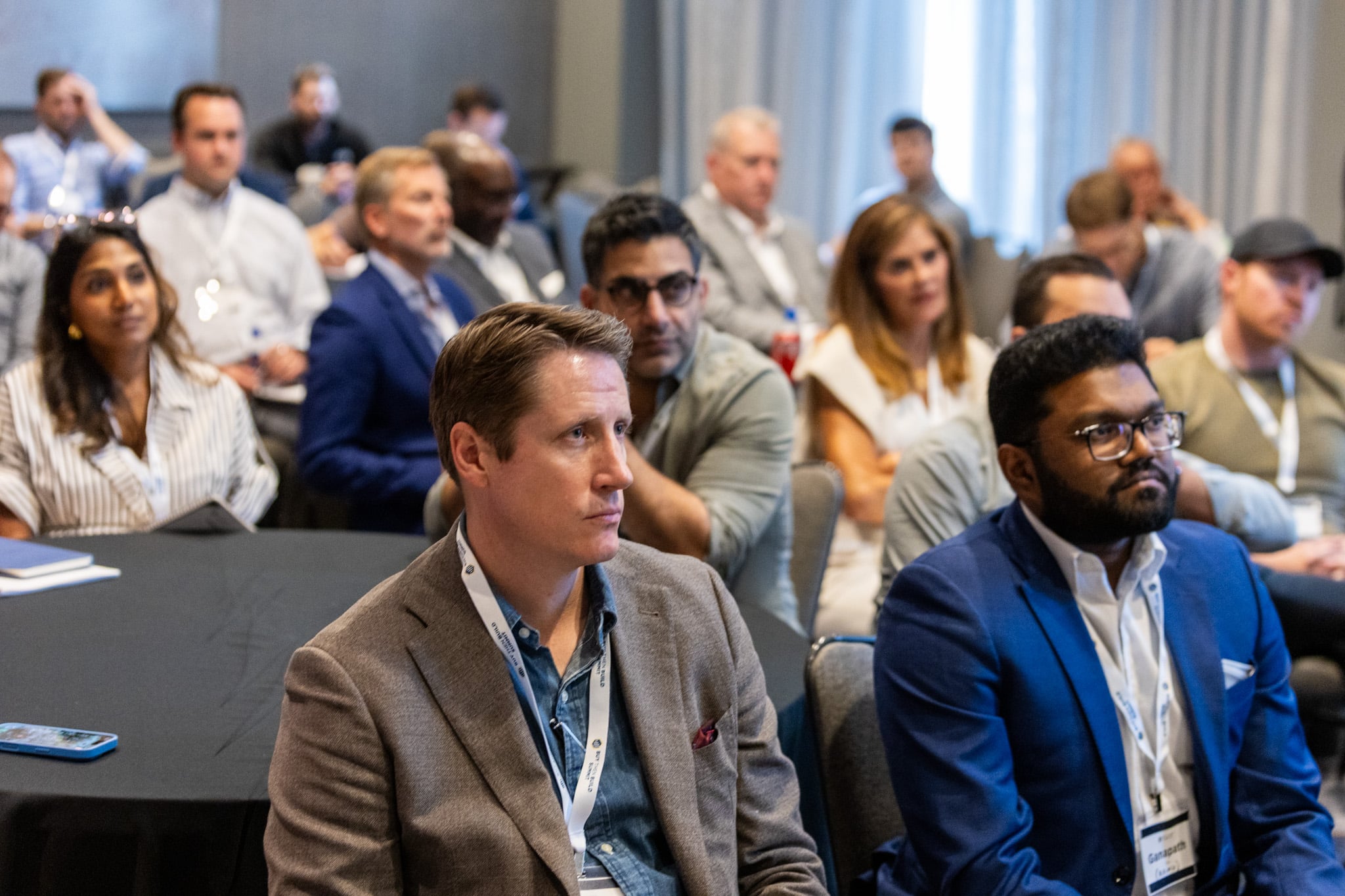 Attendees at an Acquisition Lab summit session, seated at round tables and listening to a speaker